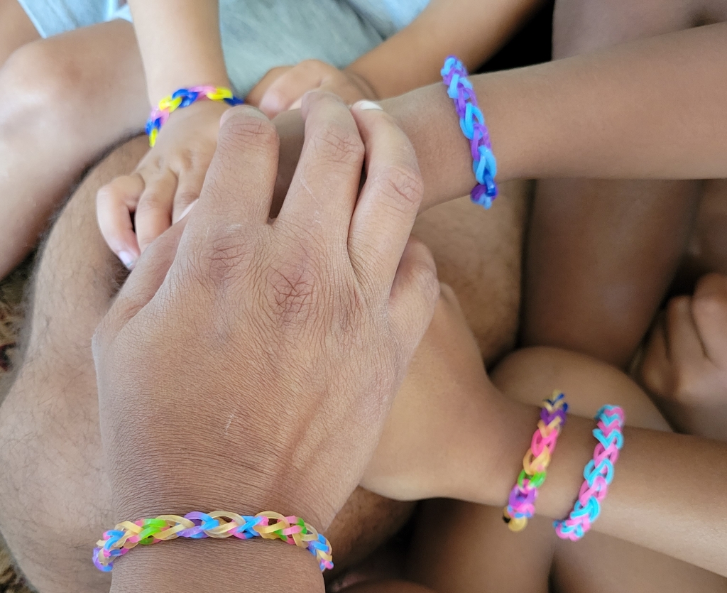 A bunch of hands all clasped together wearing colorful bracelets.