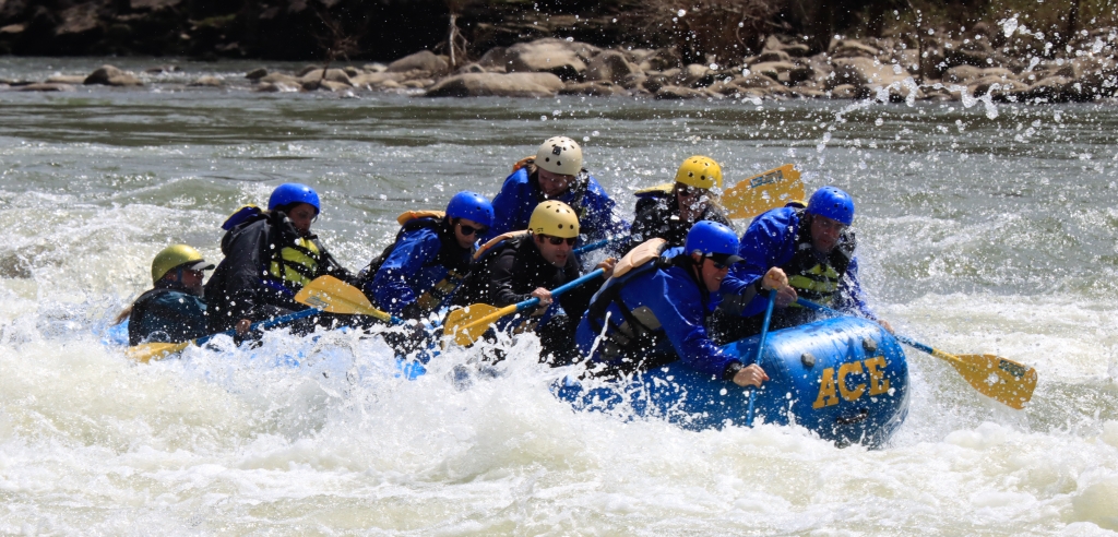 A group of people on an inflateable raft that is blue with yellow paddles.