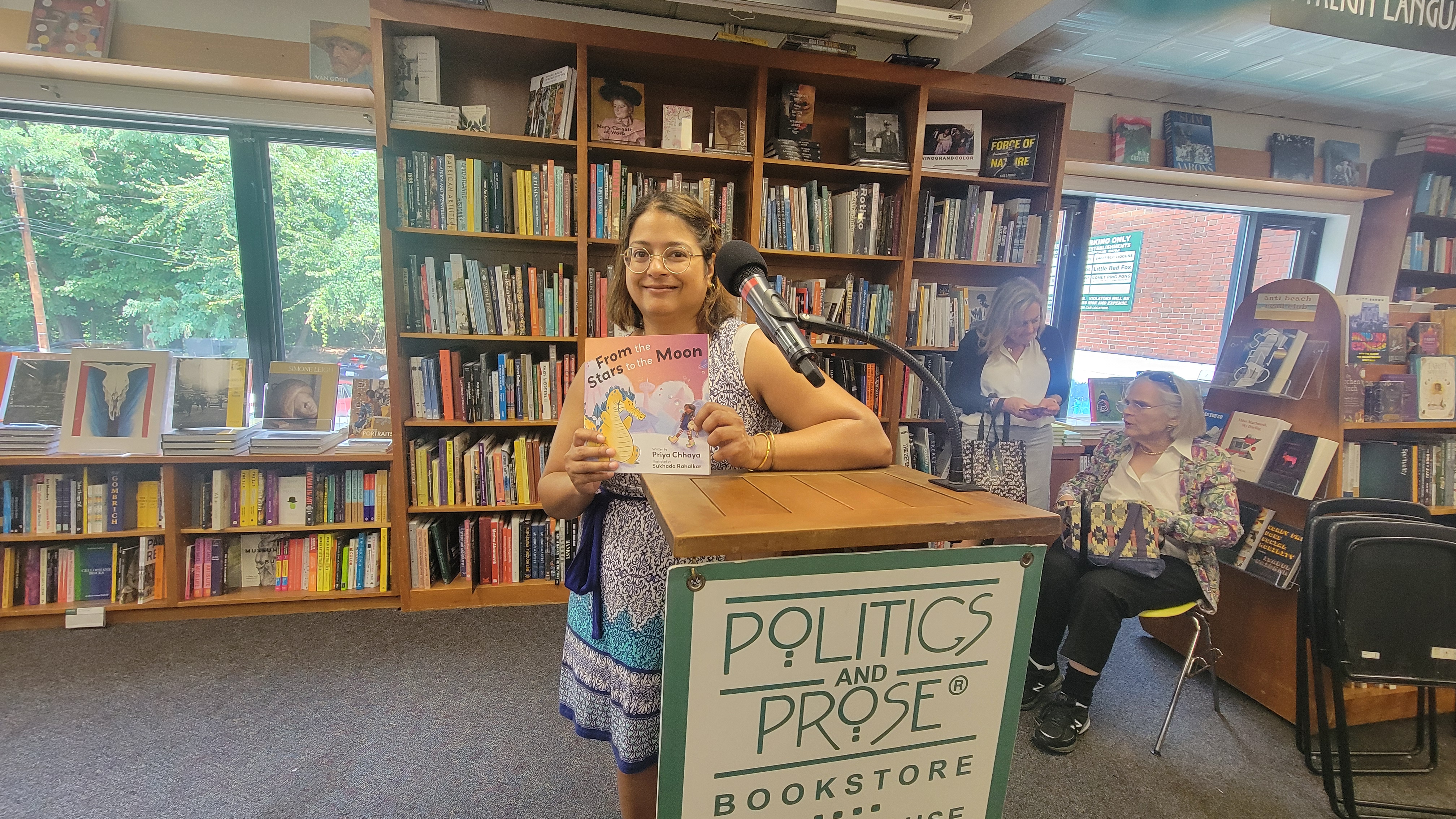 A woman at a podium holding a book "From the Stars to the Moon." with a smile.