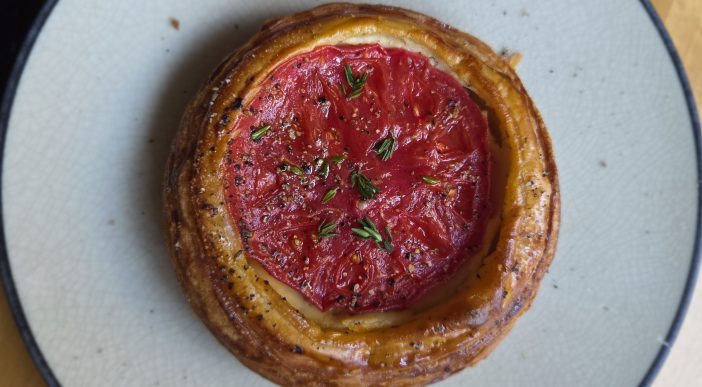 A round pastry with a round tomato on a circular gray plate.
